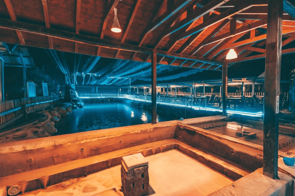 【六龜住宿】高雄六龜【草地人Spa民宿】露天溫泉區夜景，木造屋頂結構與池畔燈光交織出溫暖氛圍，適合夜晚放鬆泡湯、欣賞夜色景觀。