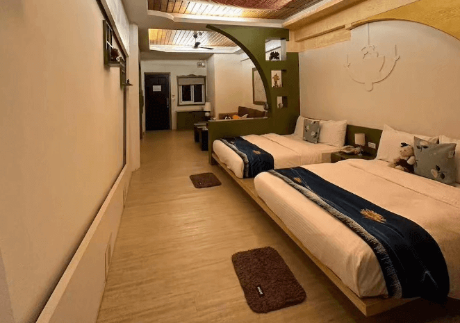 【六龜住宿】高雄六龜【道時尚悠然山莊】現代風雙床房，採用溫潤木地板與綠色弧形隔牆設計，房內配有沙發區與床邊小飾品，營造溫馨療癒感。