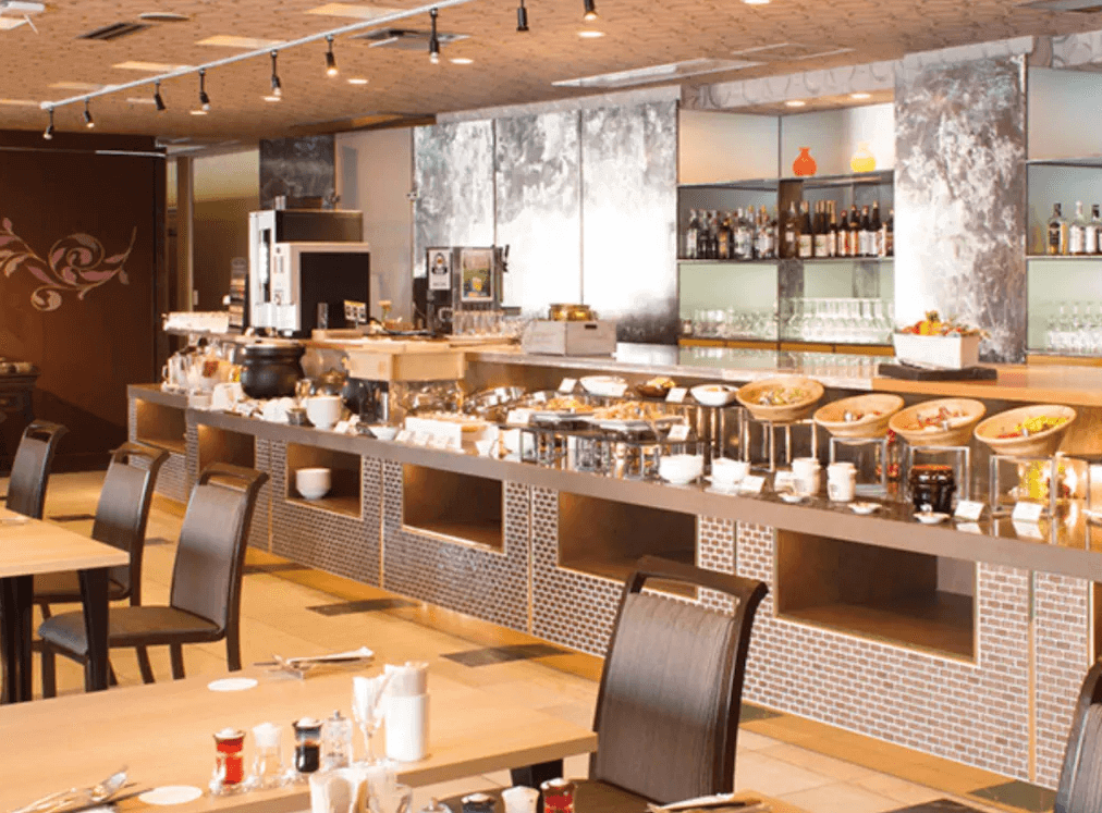 【釧路住宿】釧路世紀城堡飯店自助餐廳早餐區，餐檯上擺滿多樣料理與飲品，現代化裝潢搭配溫暖燈光，營造高雅用餐氛圍。