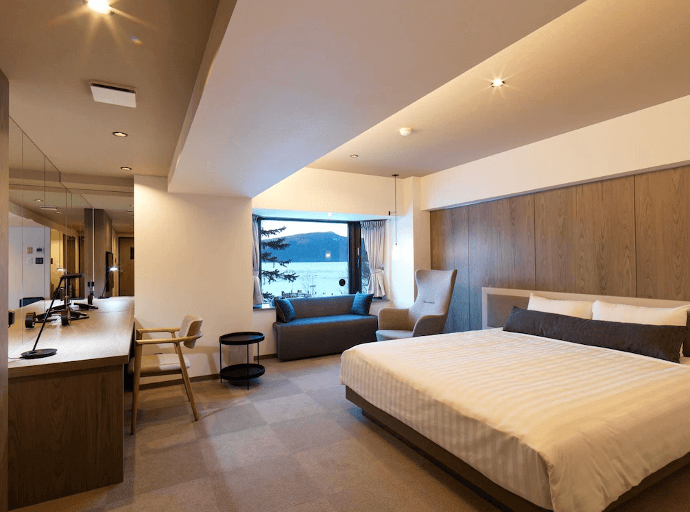 【釧路住宿】阿寒之森鶴雅度假村湖景客房，設有大面窗景可欣賞阿寒湖美景，房內以自然木質調設計，配置舒適大床與沙發椅，氛圍寧靜放鬆。