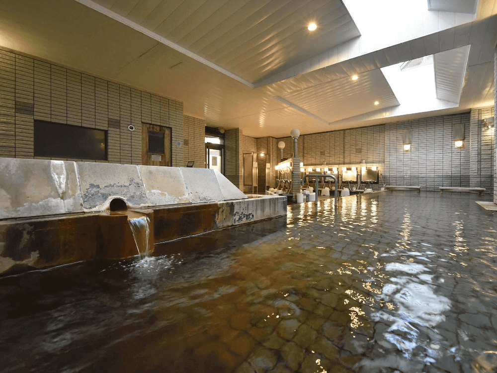 【釧路住宿】阿寒之森鶴雅度假村室內溫泉浴場，以石材與木質結構打造，溫泉水潺潺流動，空間寬敞明亮，展現日式溫泉質感。