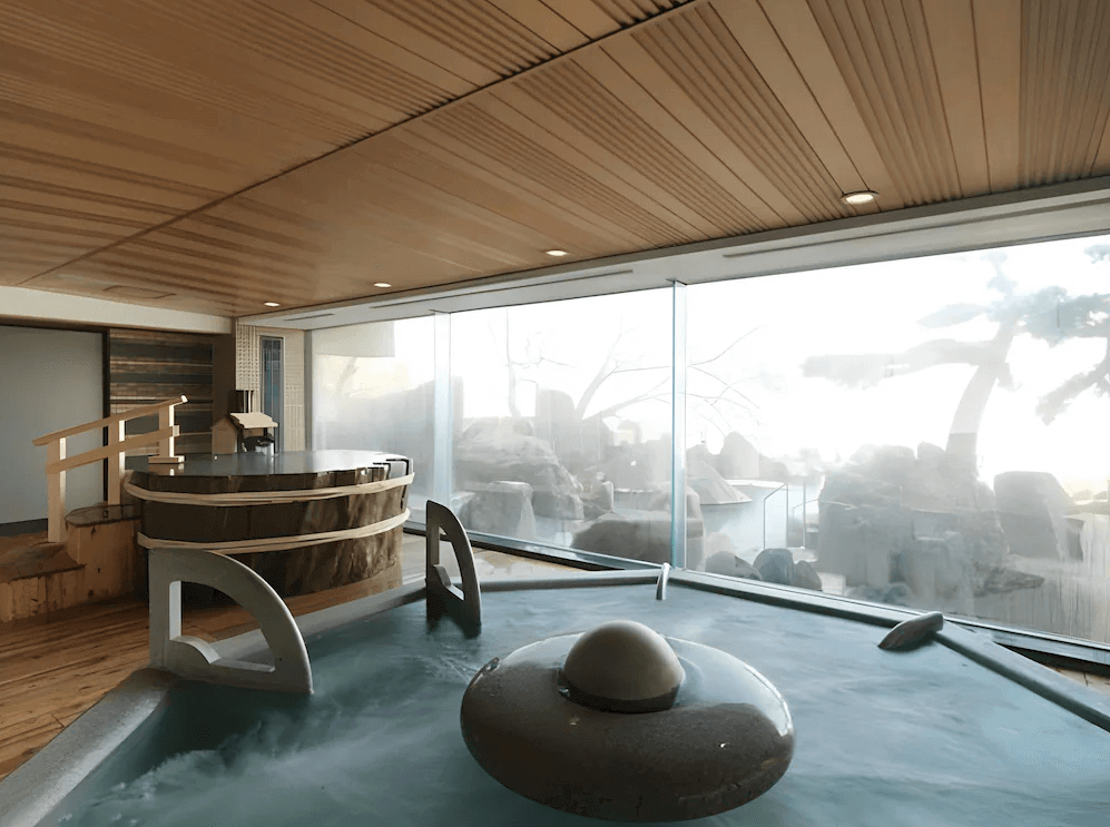 【釧路住宿】阿寒遊久之里鶴雅館內溫泉浴池，設有木桶風呂與大型泡湯池，透過落地窗可欣賞自然景觀，提供絕佳的泡湯體驗。