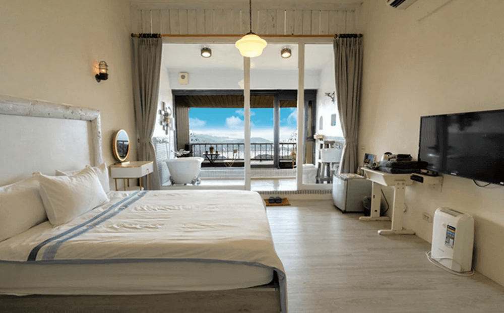 【瑞芳住宿】陽光味宿｜海景雙人房設計明亮寬敞，房內白色基調搭配落地窗外的藍天海景，並設有復古浴缸與陽台，展現浪漫地中海氛圍。