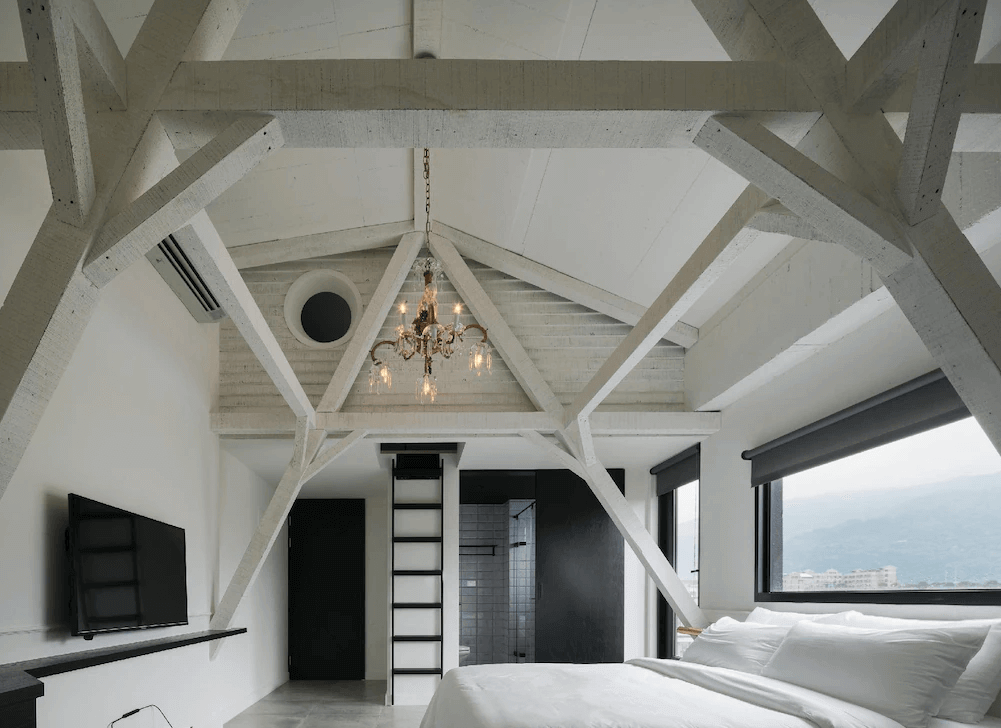 【頭城住宿】宜蘭黑宅 Black House 閣樓房型，白色屋樑結構設計與挑高天花板，搭配復古吊燈與大片採光窗，展現簡約又高雅的空間感。