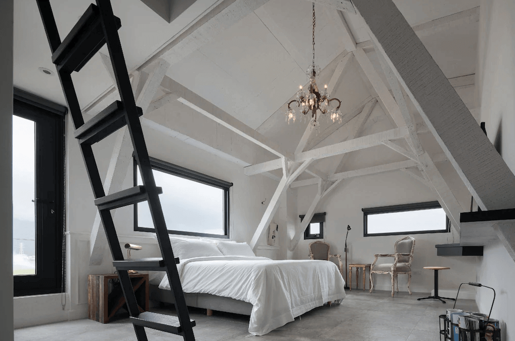 【頭城住宿】宜蘭黑宅 Black House 閣樓套房，白色樑柱結構與斜屋頂設計，配有雙人床、復古椅與黑色階梯，整體空間明亮寬敞。