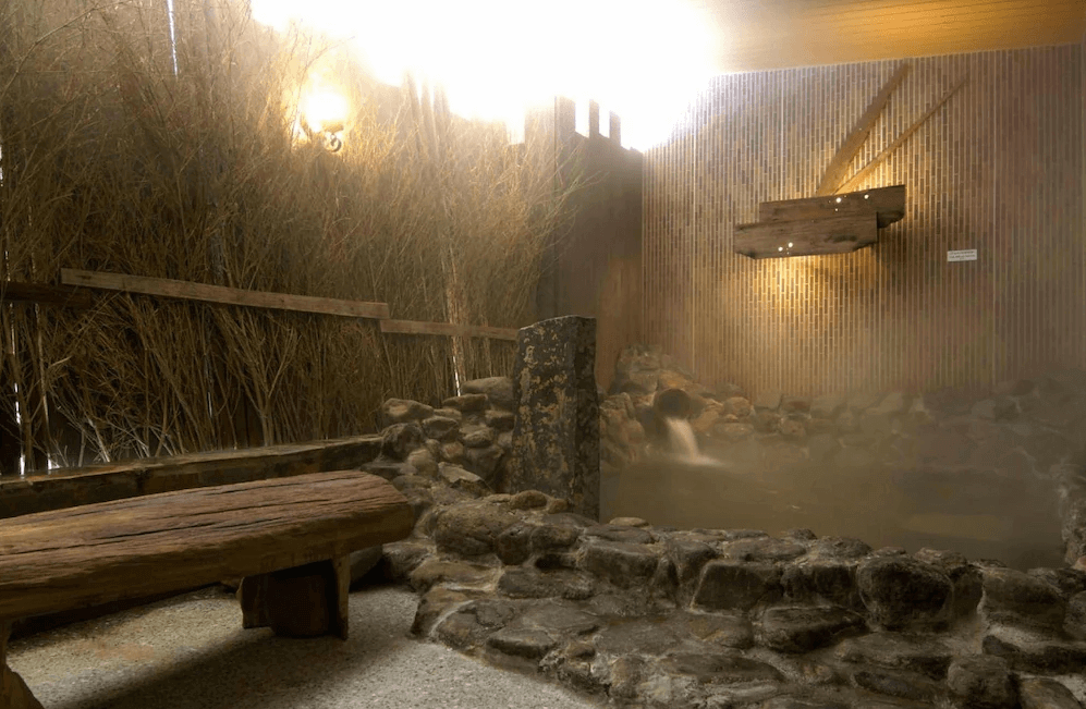 【北見住宿】Dormy Inn Kitami 北見飯店的溫泉浴池區，以石造池與竹籬圍繞，充滿自然氣息，蒸氣瀰漫營造放鬆療癒的泡湯環境。