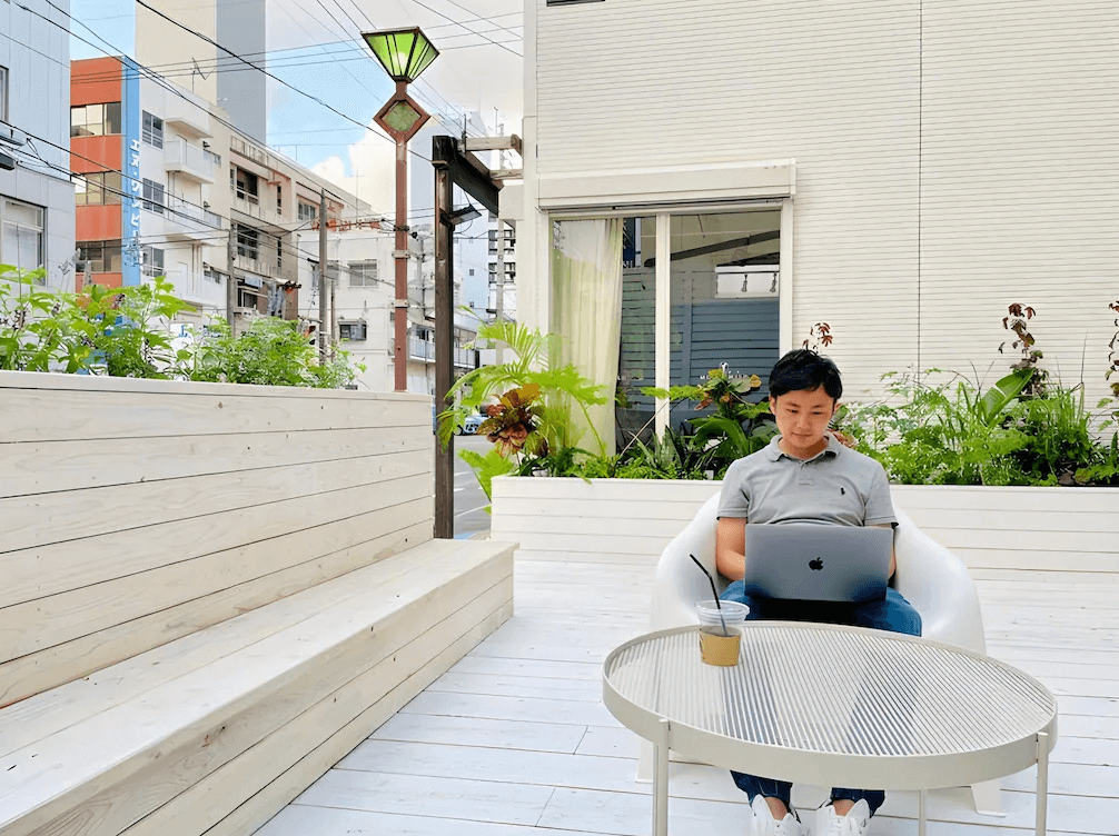 【奄美大島住宿】「En-Hostel & Café Bar 戶外露台：白色木質平台搭配植栽綠意，旅客可在戶外座椅上使用筆電或享用飲品，環境清爽舒適。」