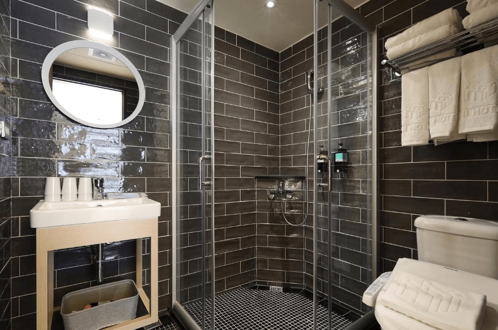 【台中火車站住宿】「MINI HOTELS 台中火車站館的衛浴空間，搭配深色磚牆、乾濕分離淋浴間與大面圓鏡，整體設計現代且功能完善。」