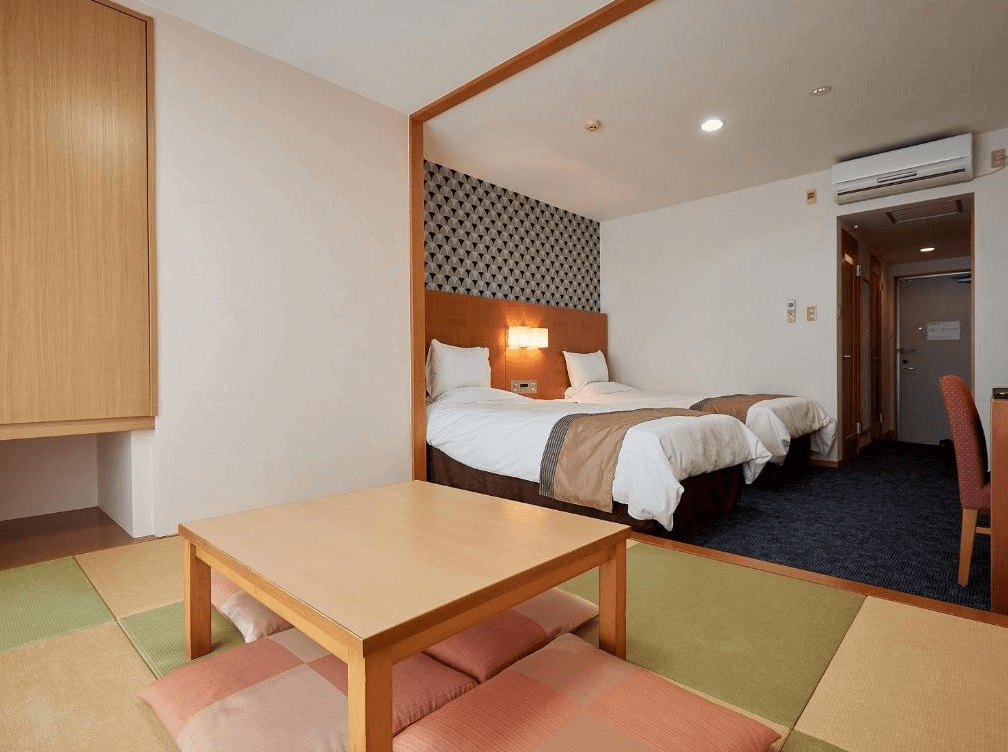 【讀谷村住宿】「Murasakimura 飯店的和洋合併客房，前方為榻榻米座位區，後方為兩張單人床，整體空間寬敞，提供家庭旅客舒適的住宿體驗。」