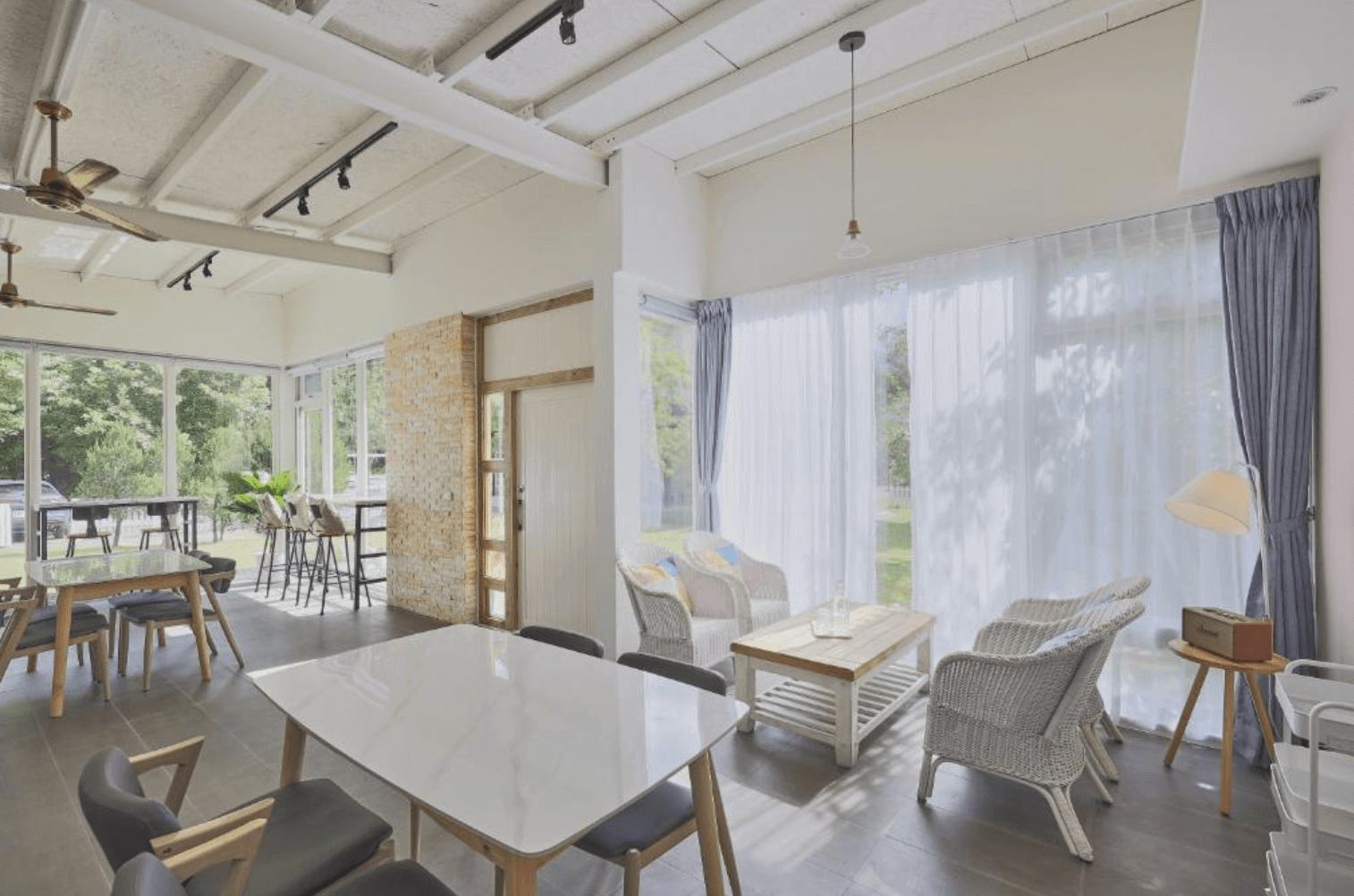 【東華大學民宿】「OwlStay故事所 綠舍」公共交誼廳，大片玻璃窗採光充足，室內以白色與木質調營造自然氛圍，設有餐桌與藤編座椅，適合親友聚會與放鬆。