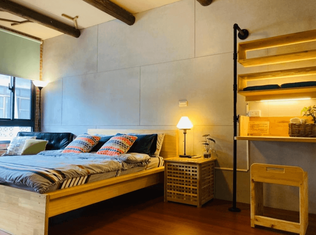【大溪住宿】「湧山水民宿 Sinnan 12 Homestay — 溫馨雙人房，木質床架與柔和燈光營造舒適氛圍，設有書桌與層架，展現自然簡約的設計風格。」