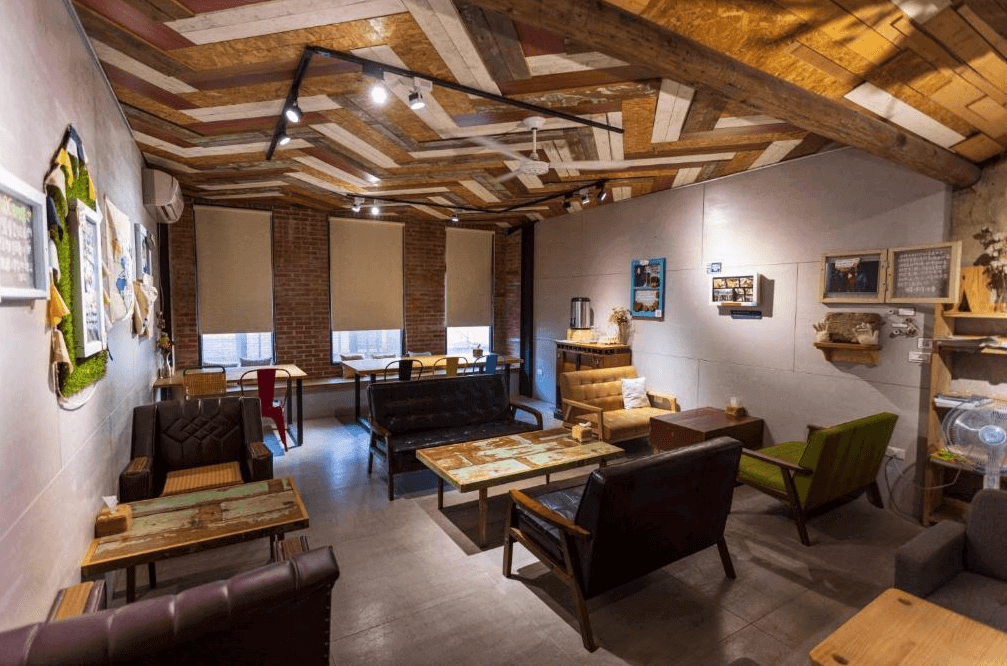 【大溪住宿】「湧山水民宿 Sinnan 12 Homestay — 公共休憩空間採用復古混搭風，木質天花板與磚牆結合，多款沙發與手作桌椅，營造自在溫暖的社交氛圍。」