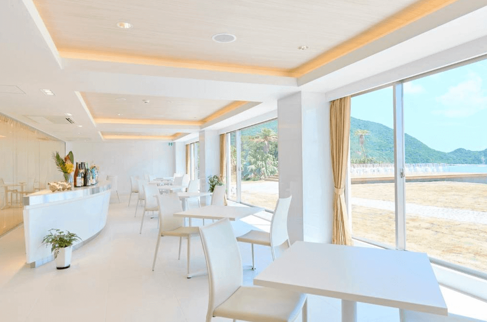【奄美大島住宿】「THE SCENE 奄美 Spa 度假村餐廳：潔白明亮的用餐空間配上全景落地窗，可俯瞰海灘與翠綠山景，營造清爽舒適的海島度假氛圍。」
