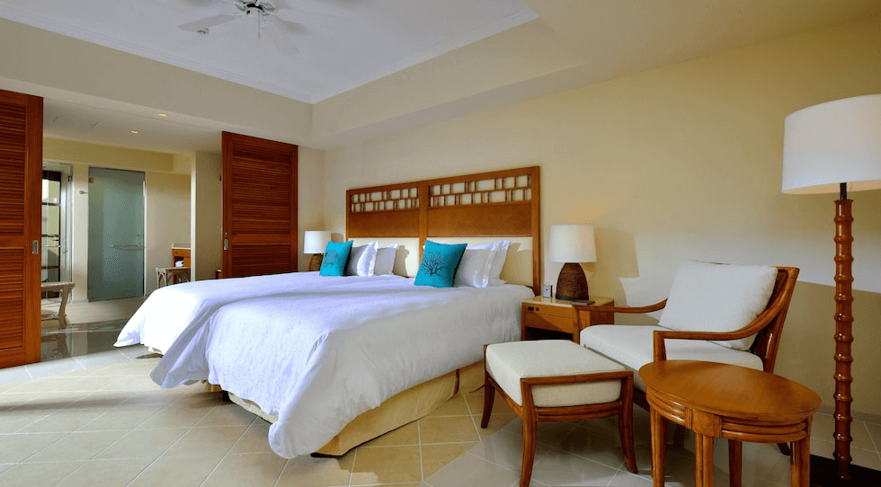 【讀谷村住宿】「The Uza 露台海灘俱樂部別墅的雙床臥室，採用溫暖的木質家具與米白色系，搭配湖水綠抱枕，營造度假般的清新舒適氛圍。」