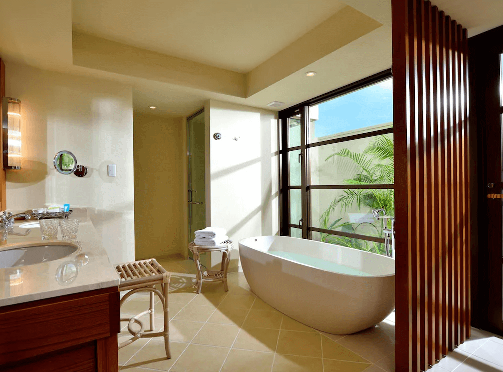 【讀谷村住宿】「The Uza 露台海灘俱樂部別墅的明亮浴室空間，設有大型獨立浴缸、木質拉門與大片窗景，可眺望庭院綠意，呈現高雅度假風格。」