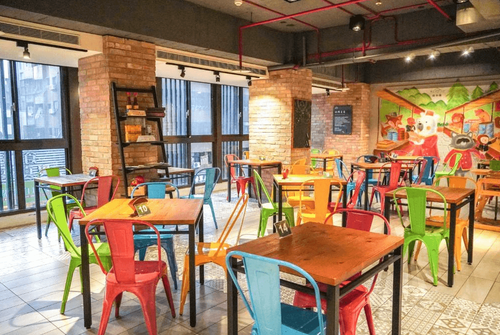 【台中火車站住宿】「old school 行旅・田中央旅店的用餐空間，以工業風磚牆、彩色金屬椅與手繪插畫牆裝飾，營造活潑年輕的聚餐氛圍。」