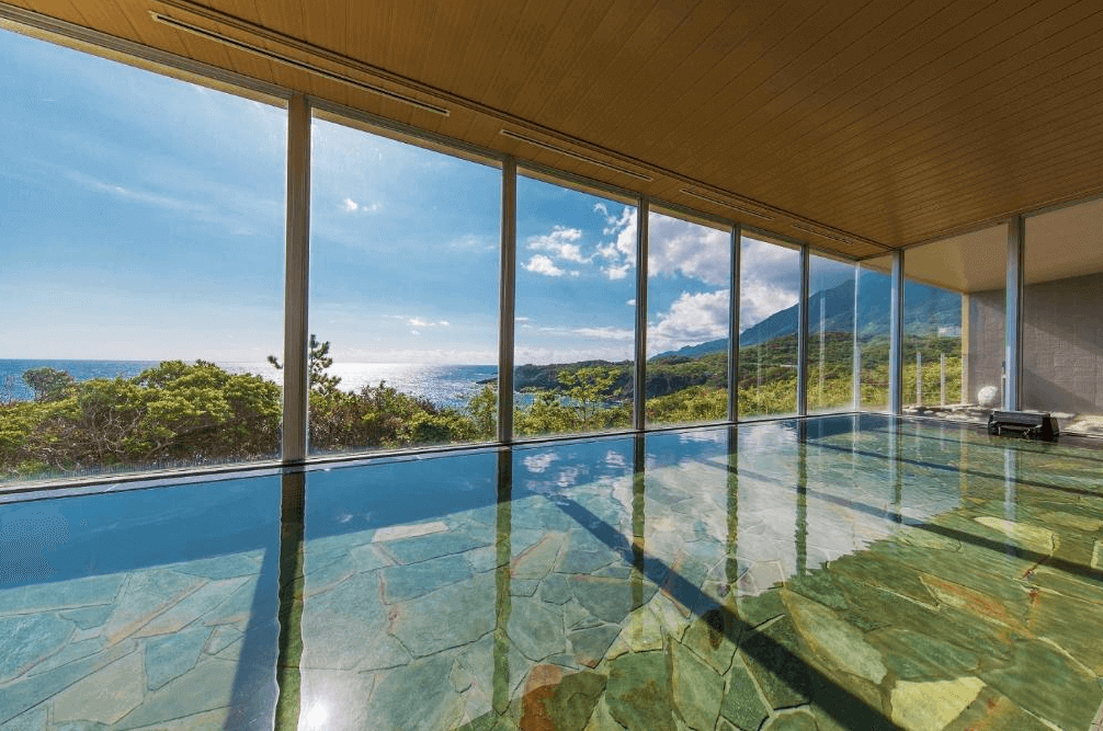 【屋久島住宿】「samana hotel Yakushima 薩馬納飯店屋久島的景觀大浴場，擁有寬闊落地窗，可同時欣賞海景與山景，石材浴池設計自然清新，是旅館的亮點設施之一。」