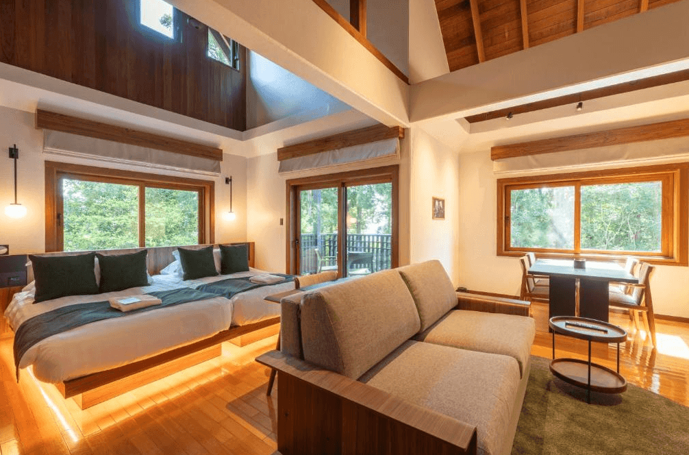 【屋久島住宿】「三卡拉羅久島Spa酒店 Sankara Hotel & Spa Yakushima 的森林系雙人房，採挑高木質設計，大片落地窗可欣賞樹林景色，房內設有沙發與用餐區，空間寬敞明亮。」