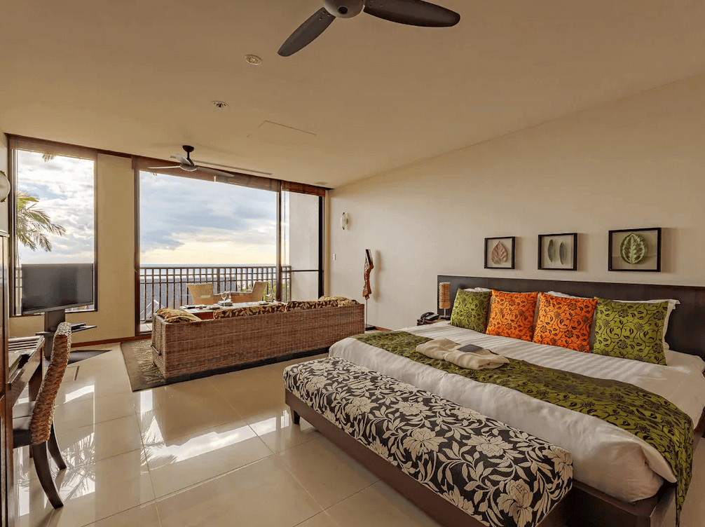 【屋久島住宿】「三卡拉羅久島Spa酒店 Sankara Hotel & Spa Yakushima 海景客房，房內配置特大床與藤編沙發區，透過落地窗可眺望太平洋夕陽海景，房間風格溫暖放鬆。」