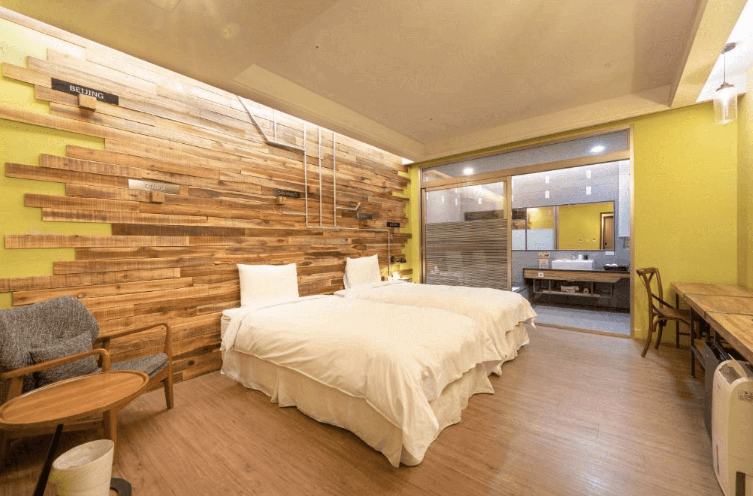【宜蘭溫泉飯店】「九號溫泉旅店雙床房，以木質牆面拼接與暖黃色調打造自然溫馨氛圍，房內配置休憩座椅與透明玻璃隔間浴室，空間寬敞舒適。」