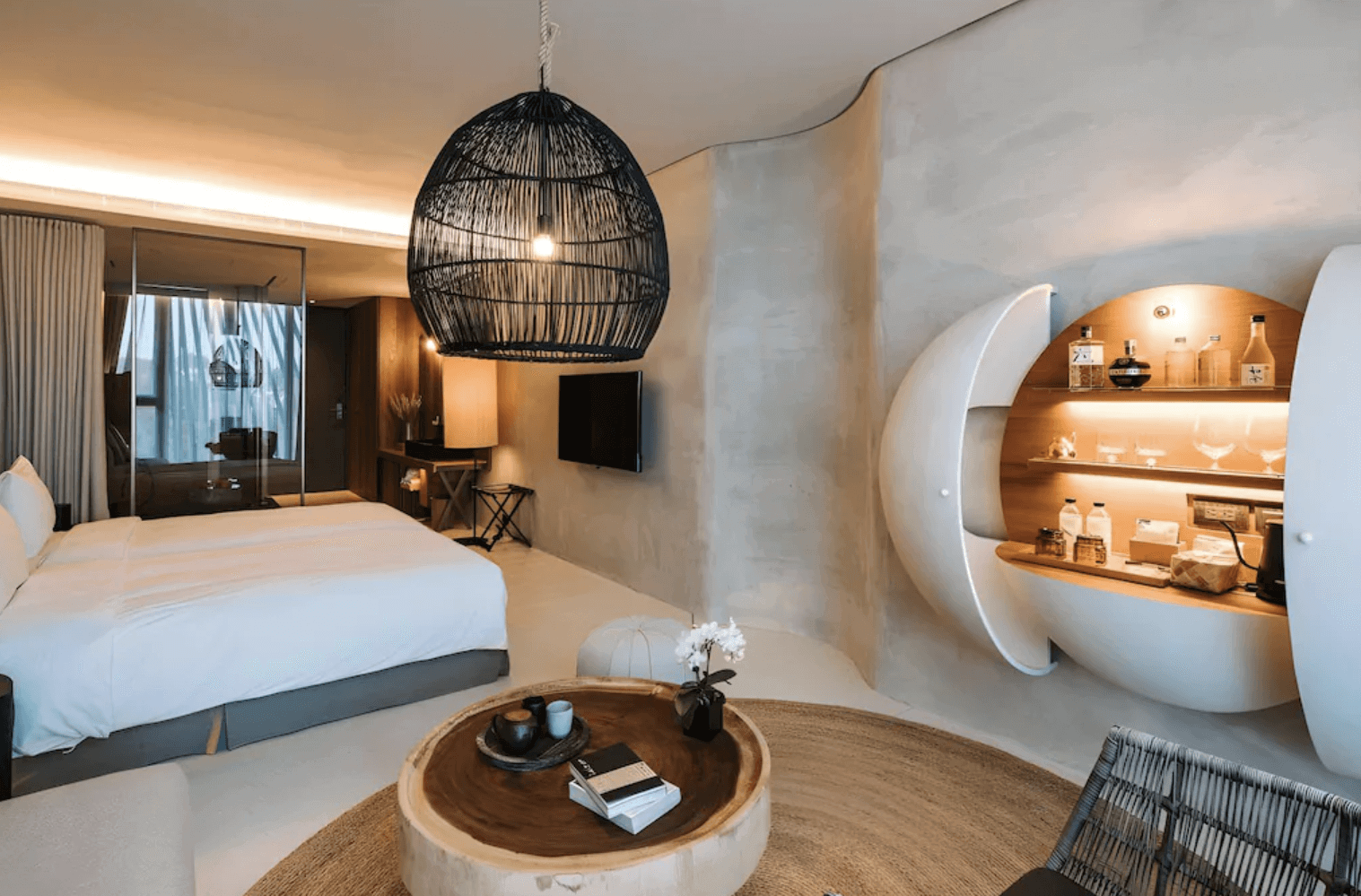 【宜蘭溫泉飯店】「了了礁溪 VIVIR Jiaoxi 客房內景，室內以自然泥灰質感牆面、圓形木桌與大型編織吊燈營造質感設計感，房內設有舒適大床與半圓形展示酒櫃，空間溫暖且富有風格。」
