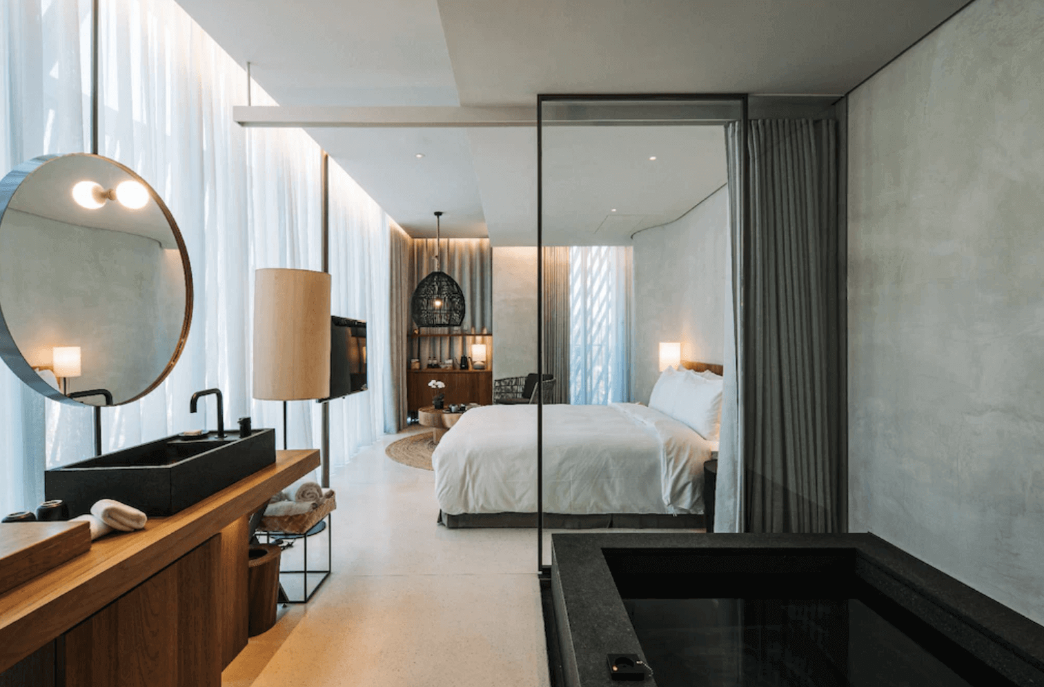 【宜蘭溫泉飯店】「了了礁溪 VIVIR Jiaoxi 客房全景，從浴室望向臥室的開放式設計，大面窗簾採光柔和，搭配深色洗手台與木質元素，營造現代又帶有自然氣息的住宿氛圍。」