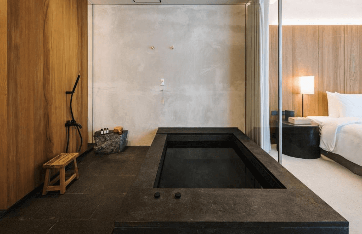 【宜蘭溫泉飯店】「了了礁溪 VIVIR Jiaoxi 房內溫泉浴池與淋浴空間，深色石材打造的大型泡湯池緊鄰木質牆面與玻璃隔間，展現低調奢雅的日式溫泉風格。」