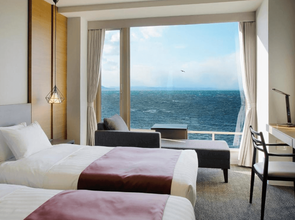 【北見住宿】佐呂間湖鶴雅度假飯店的湖景雙床房，兩張單人床搭配暖色床巾，窗外可欣賞佐呂間湖的壯麗湖景與藍天，房間採光充足、氣氛靜謐。