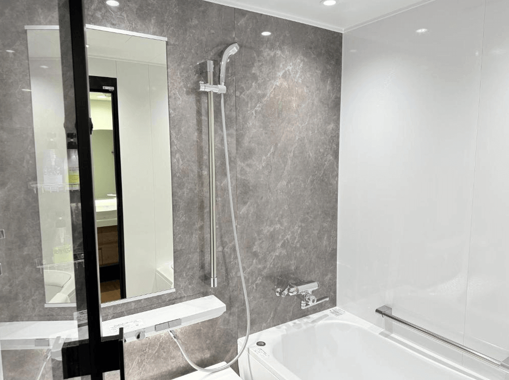 【北見住宿】佐呂間湖鶴雅度假飯店的浴室空間，採用灰白大理石紋牆面與白色浴缸，配有淋浴設備與鏡面設計，整體乾淨明亮、質感高雅。