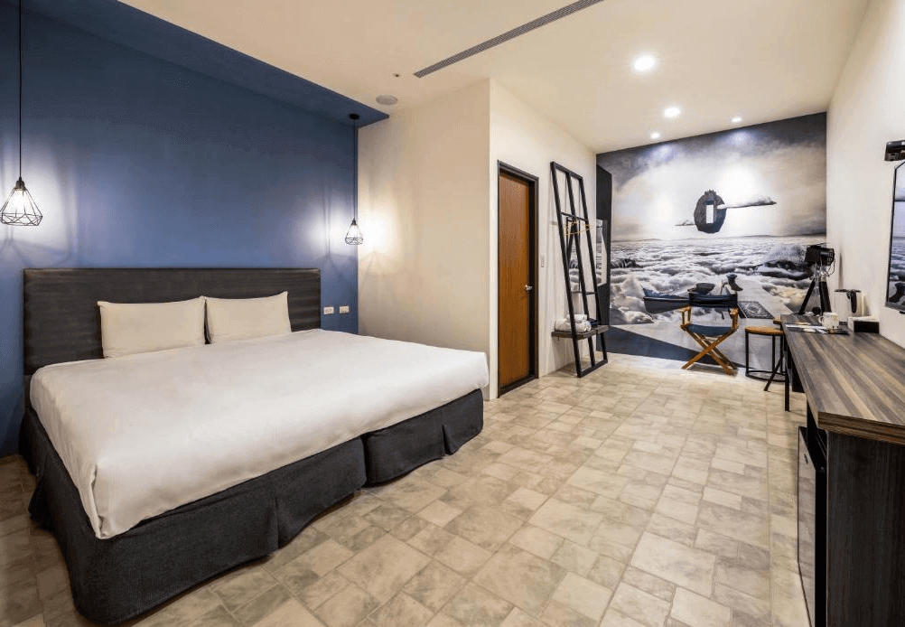 【台中火車站住宿】「凝萃文旅台中車站店的大床客房，設有深藍色主題牆、簡約吊燈、大片床鋪與寬敞活動空間，牆面藝術感強烈的黑白風格壁畫增添設計感。」