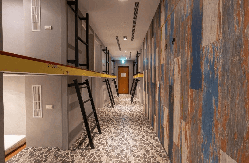 【台中火車站住宿】「凝萃文旅台中車站店的背包客膠囊區，走廊採用工業與木質混搭風格，床位以上下層設計排列整齊，並附設梯子方便上下。」