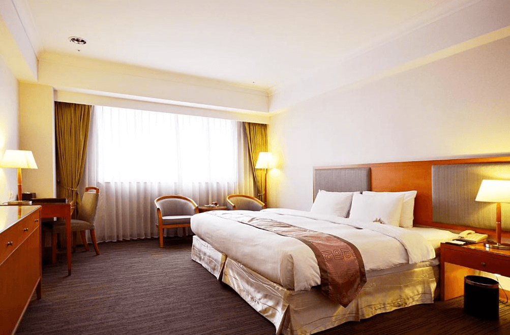 【台中火車站住宿】「台中富信大飯店的雙人客房，設有大面窗簾、暖黃色燈光與經典木質家具，房間明亮舒適，營造典雅溫馨的住宿氛圍。」