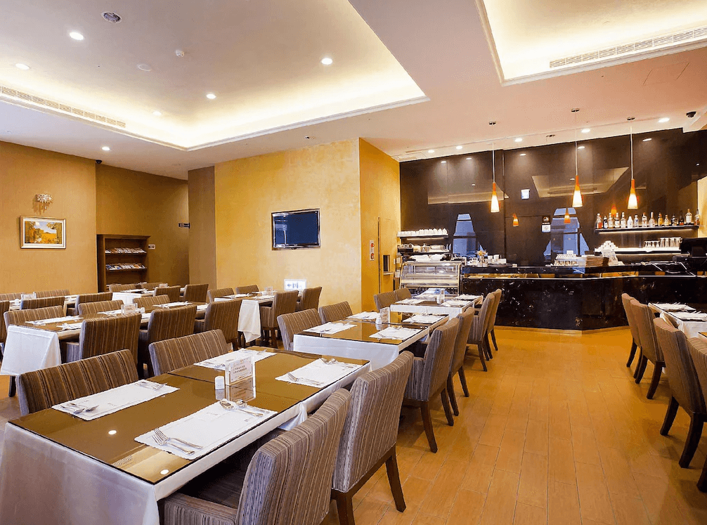 【台中火車站住宿】「台中富信大飯店的餐廳環境，設有整齊排列的用餐桌椅、暖黃色牆面與黑色大理石吧台，空間明亮舒適，提供豐富早餐與餐飲服務。」