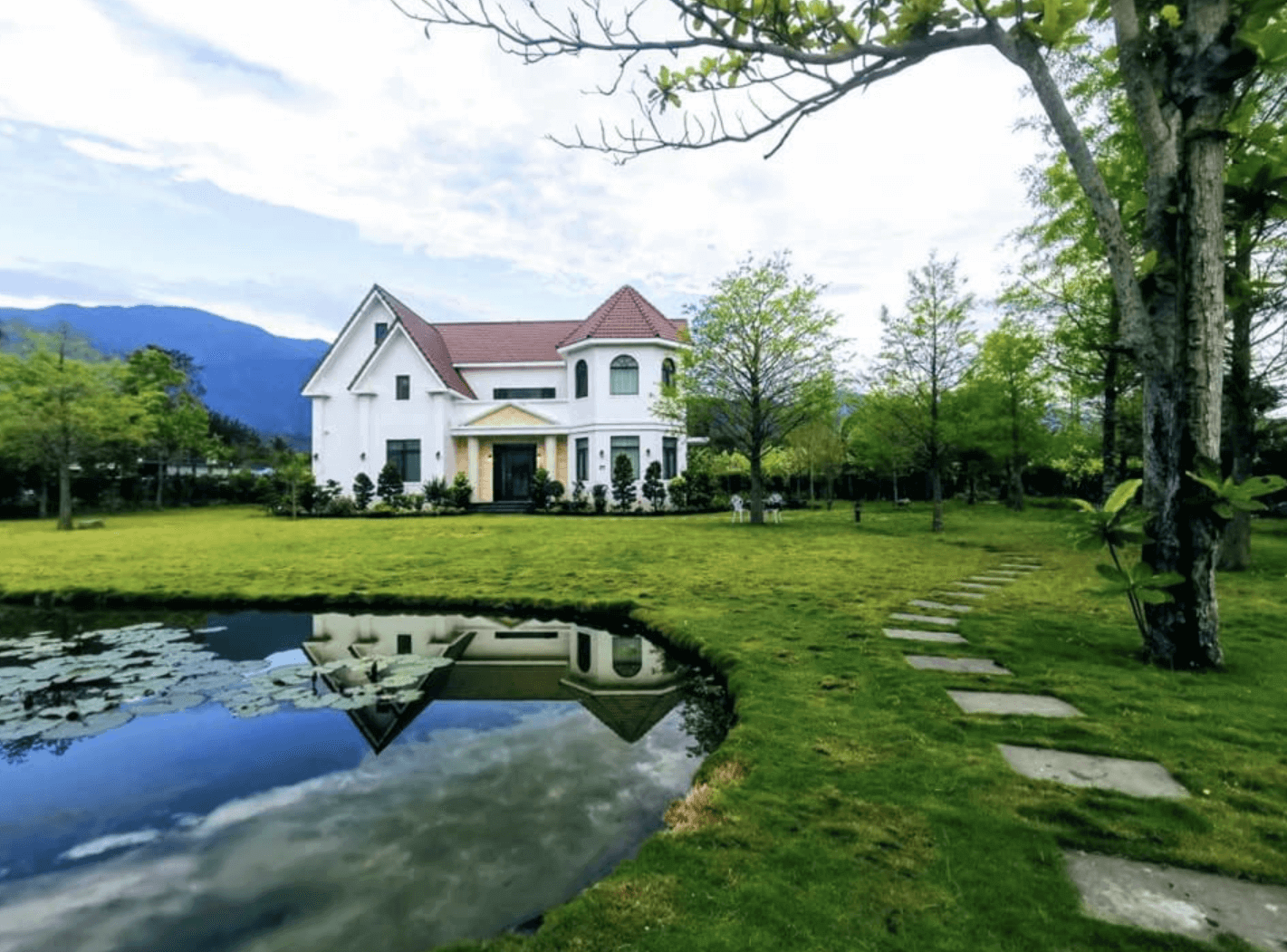 【東華大學民宿】花蓮吉哈克莊園民宿外觀，白色歐式建築坐落於綠意草坪與小池塘旁，環境清幽優美，遠眺山景如畫。