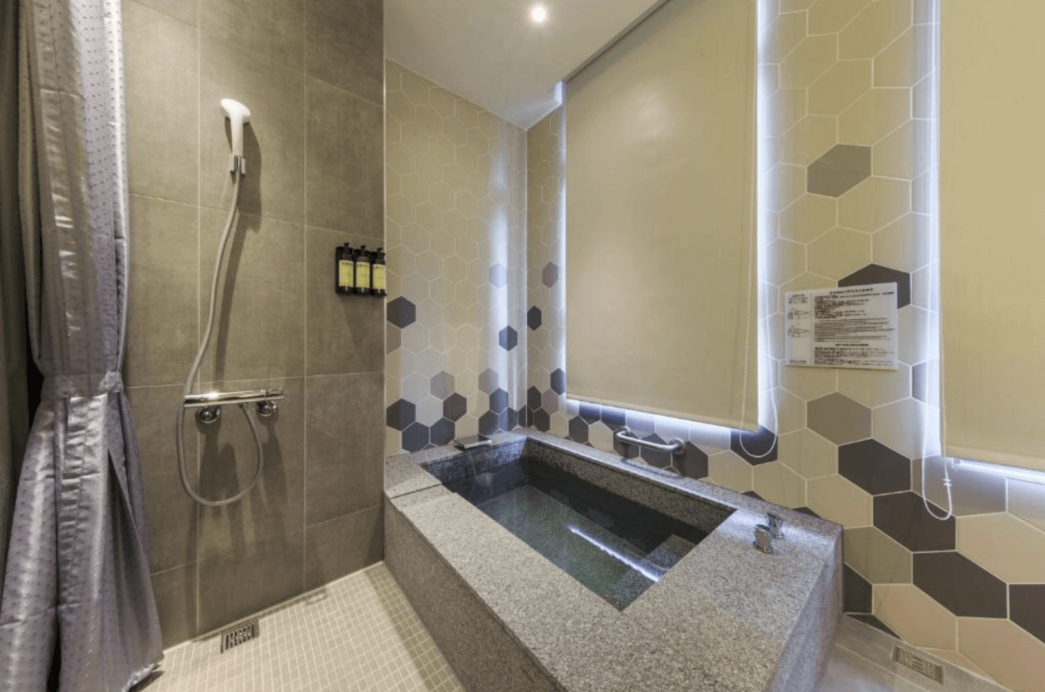 【宜蘭溫泉飯店】「品文旅客房浴室空間，設有大理石泡湯池與乾濕分離淋浴區，牆面以六角形花磚拼接設計，營造清新質感的洗浴環境。」