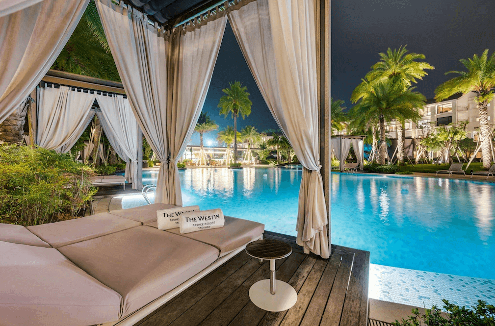 【大溪住宿】"大溪住宿精選示意圖"「大溪笠復威斯汀度假酒店 — 夜間泳池景觀，熱帶棕櫚樹環繞，設有白色帷幕躺椅與水邊涼亭，散發浪漫南洋渡假風情。」