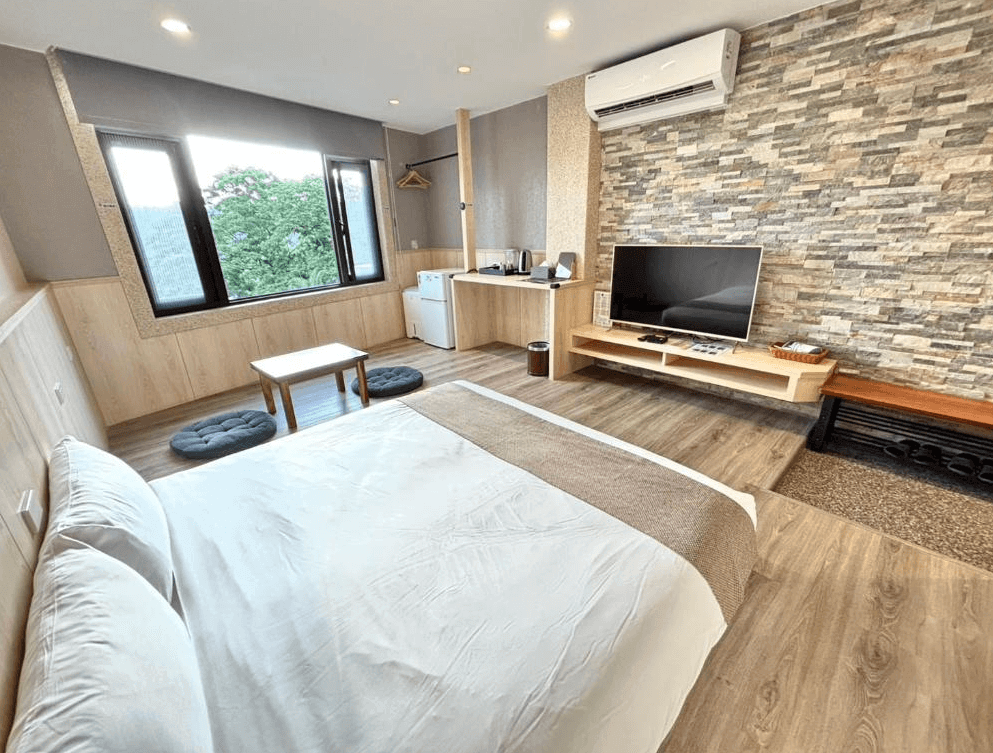 【大溪住宿】大溪老城四季行館好客民宿 山景雙人房，大片窗戶採光良好可遠眺綠意山景，設有電視、茶几與冰箱，石紋牆面營造自然質感。