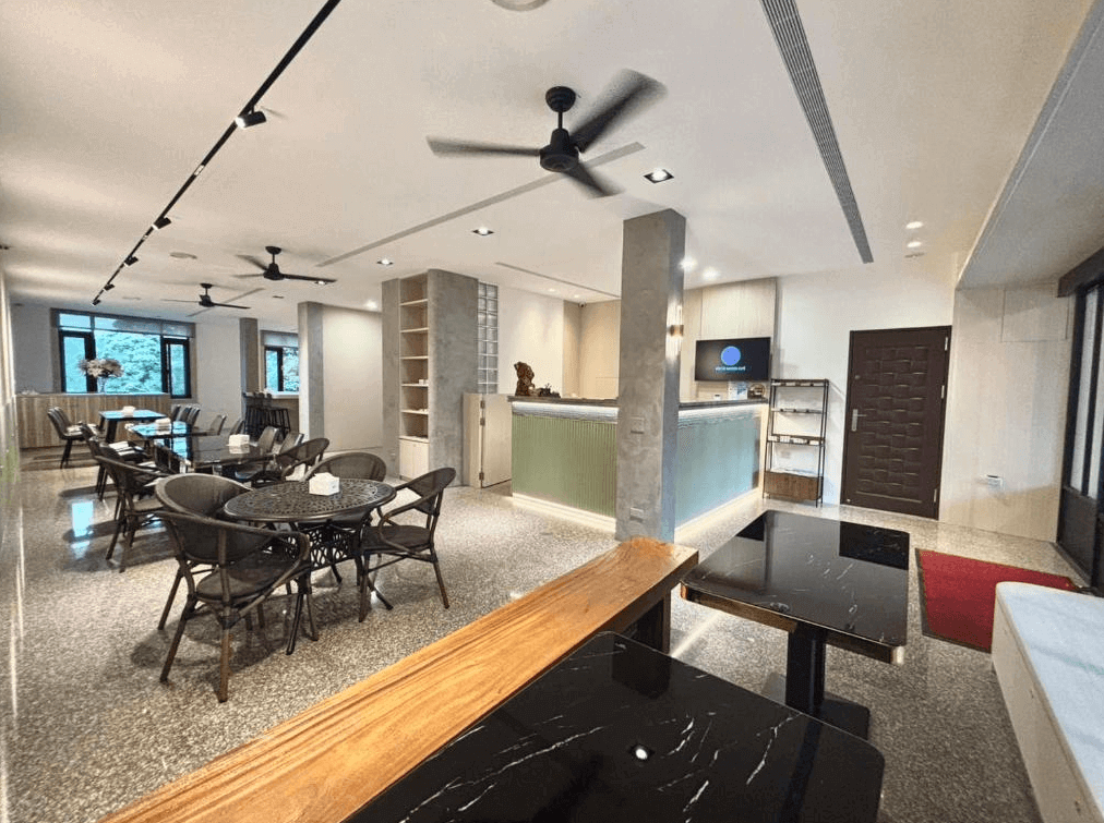 【大溪住宿】大溪老城四季行館好客民宿 大廳與用餐區，挑高空間設有多組黑色圓桌與吊扇，櫃檯設計簡約雅緻，氛圍舒適明亮。