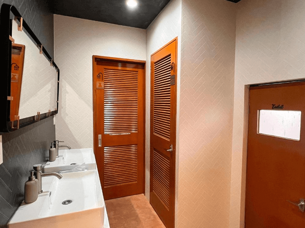 【奄美大島住宿】「奄美 JOOOY Hotel 的共用衛浴空間，設有明亮洗手台、木質門片與乾淨分明的淋浴與廁所區域。」