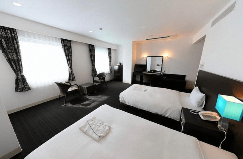 【奄美大島住宿】「奄美里貝斯特酒店（Libest Inn Amami）雙床房：寬敞明亮的客房內設有兩張單人床、休憩座椅與大片採光窗，空間舒適整潔。」