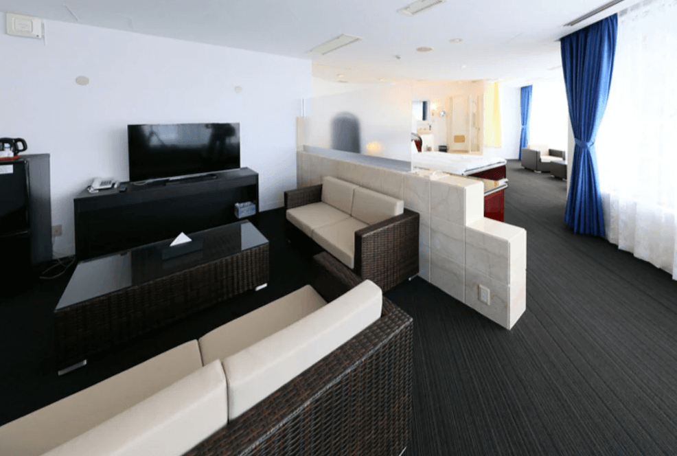 【奄美大島住宿】「奄美里貝斯特酒店（Libest Inn Amami）寬敞套房：客廳空間設有沙發、茶几與大螢幕電視，後方延伸至臥室區域，動線明亮開闊。」