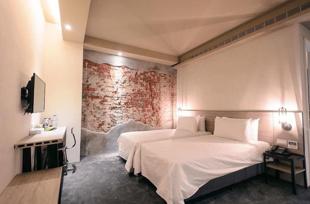 【台中火車站住宿】「奇異果快捷旅店-站前二店的雙床客房，房內以裸色與藍色為主調，牆面帶有仿舊紅磚藝術風格，空間簡約明亮，附設書桌與壁掛電視。」