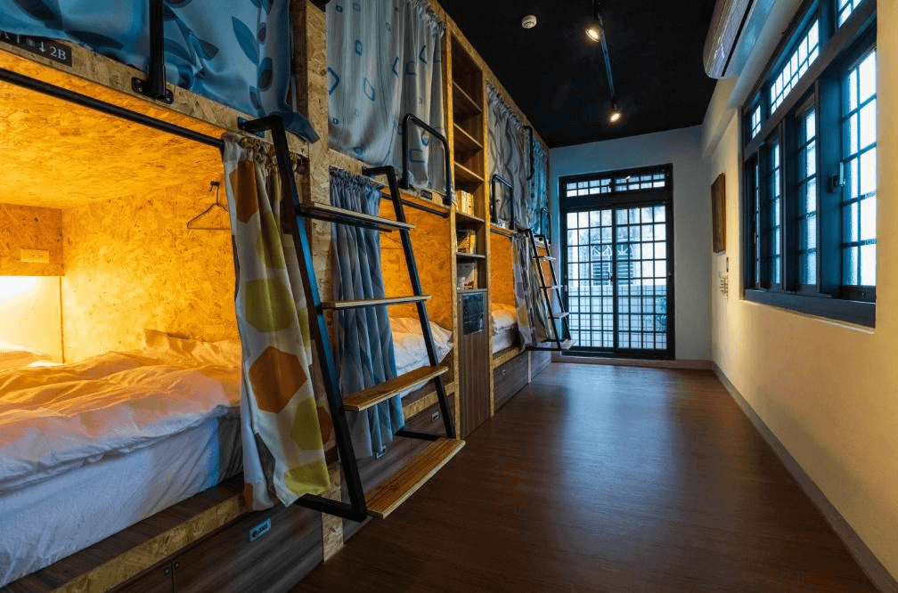 【大溪住宿】小巷內客棧 Hostel Alley Inn 膠囊宿舍房內景，木質上下舖床位搭配遮簾設計，整齊明亮的空間中有獨立照明與階梯通道，充滿文青風格。
