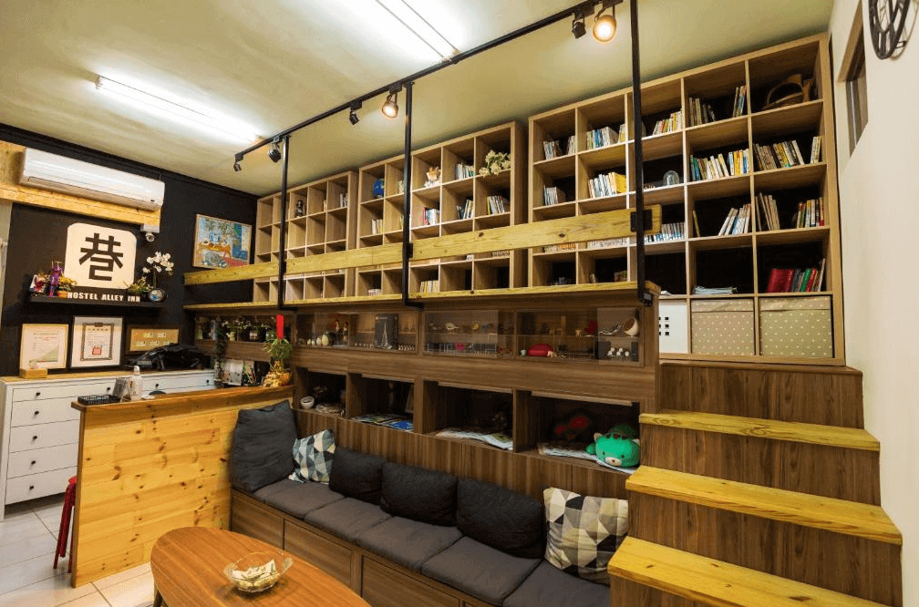 【大溪住宿】小巷內客棧 Hostel Alley Inn 交誼廳與閱讀區，溫暖木質層架陳列書籍與擺飾，沙發區舒適放鬆，整體氛圍溫馨文青。