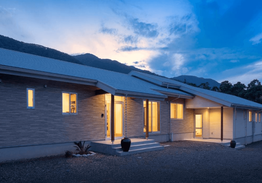 【屋久島住宿】「屋久之宿田口旅館（Yakunoyado Taguchi）外觀夜景，建築以簡約溫暖的燈光呈現，背後依傍山景，展現屋久島自然靜謐的住宿氛圍。」