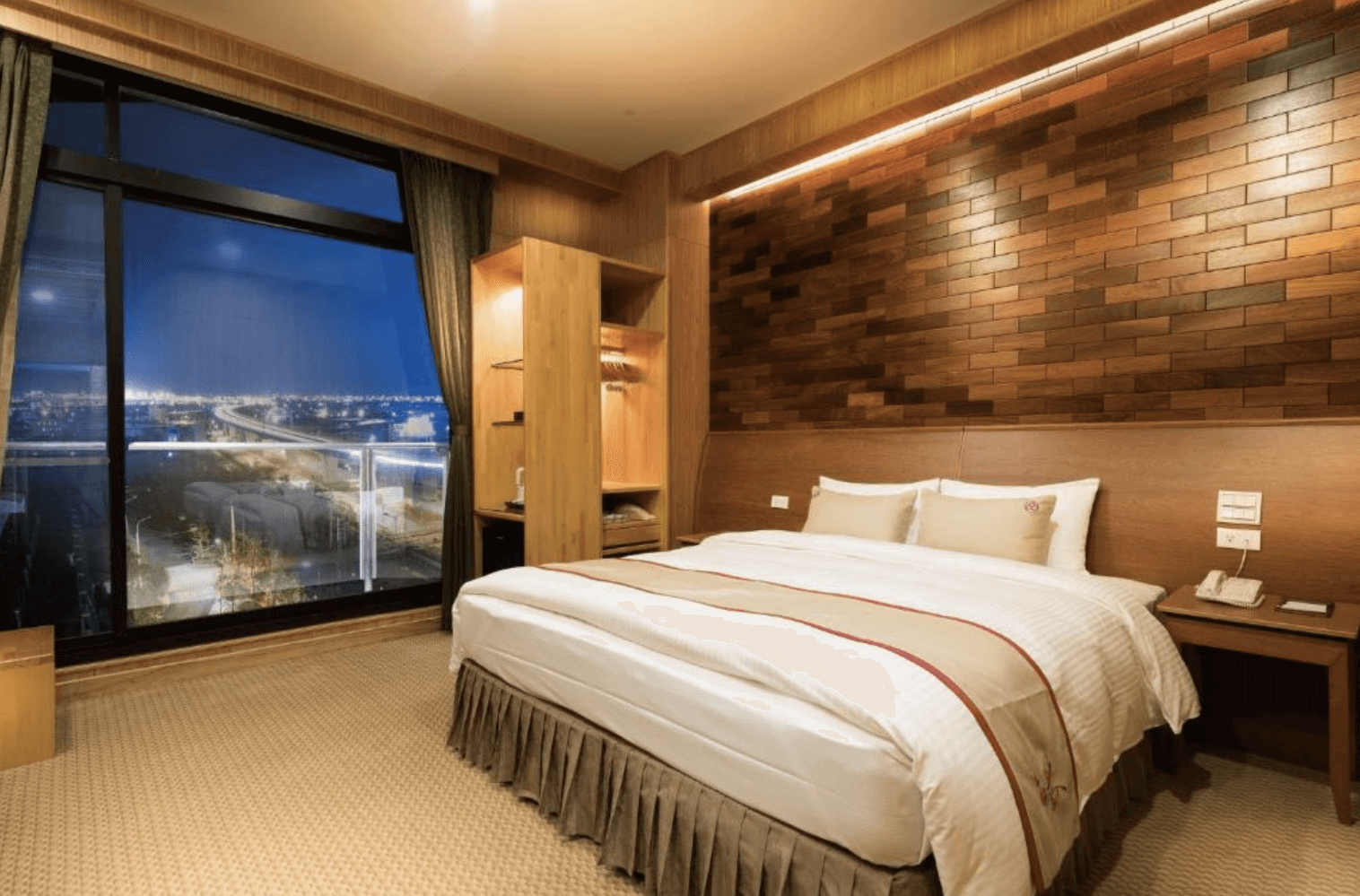 【宜蘭溫泉飯店】「山多利大飯店景觀雙人房，房內以深棕木紋牆面與暖色燈光打造沉穩質感，配置大面景觀窗可俯瞰城市夜景，大床與木質家具讓空間舒適溫馨。」