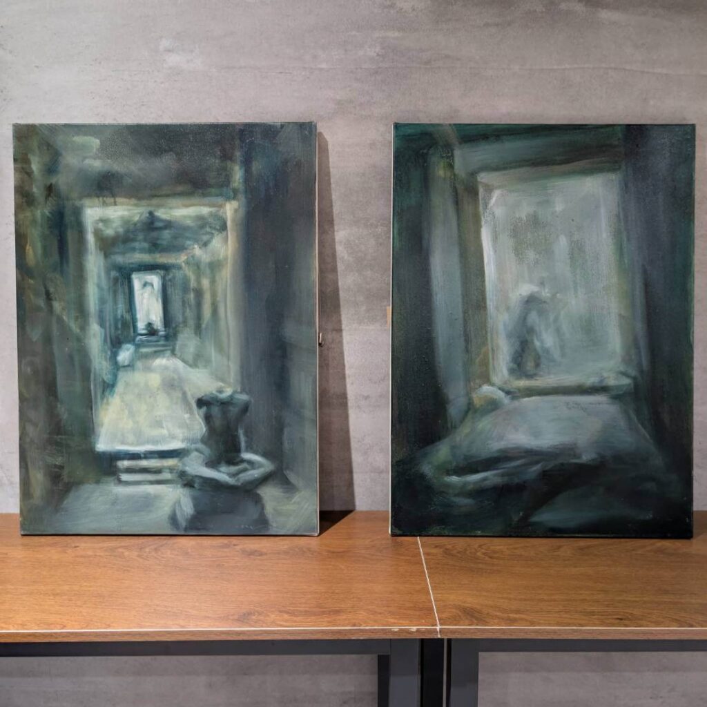 【山杉青旅】「山杉青旅大廳展示的兩幅抽象風格畫作，以灰藍與綠灰色調勾勒出朦朧的室內場景與人影，畫作置放於木質桌面前，營造文青藝術氛圍，為旅宿空間增添靜謐與神祕感。」