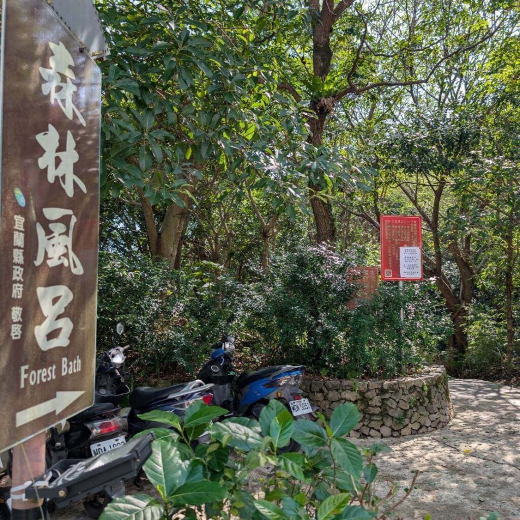 【山杉青旅】「山杉青旅周邊景點森林風呂的指標路牌立於林木間，寫有『森林風呂』字樣；周邊綠意盎然，樹木間可看到旅客停放的機車，是通往森林風呂步道的入口景致。」