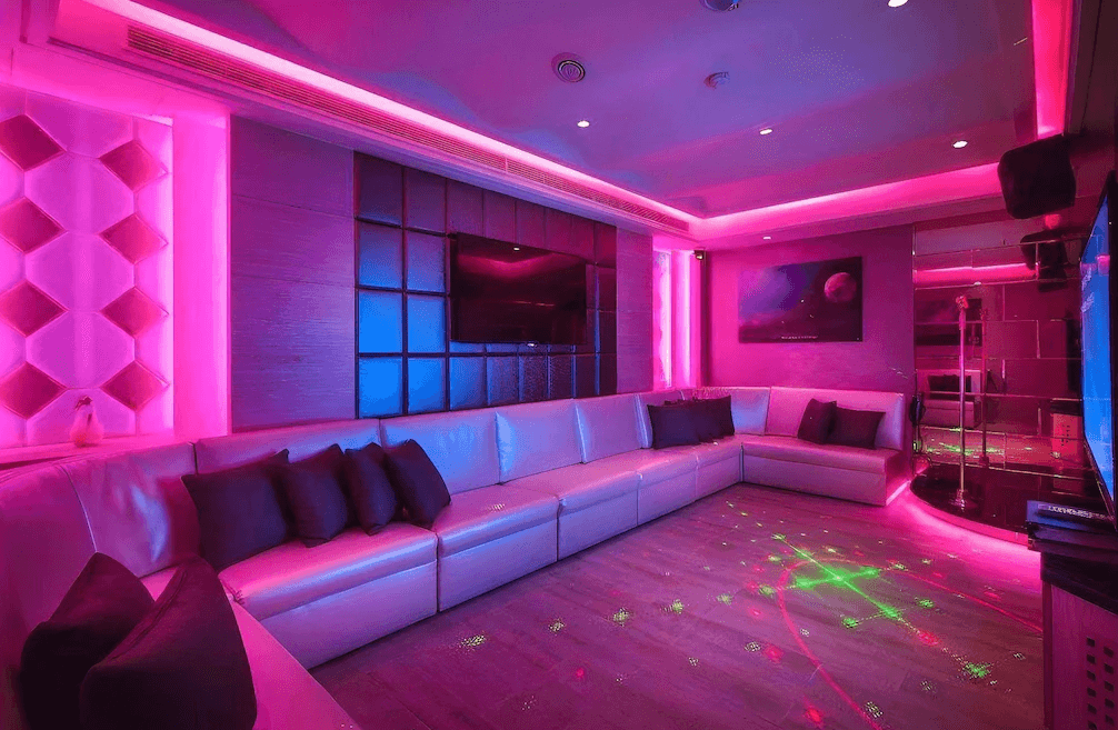 【台中火車站住宿】「承攜行旅台中自由館的KTV娛樂包廂，擁有長型白色沙發、霓虹粉紫燈光與專業音響設備，打造適合團體歡聚的華麗娛樂空間。」