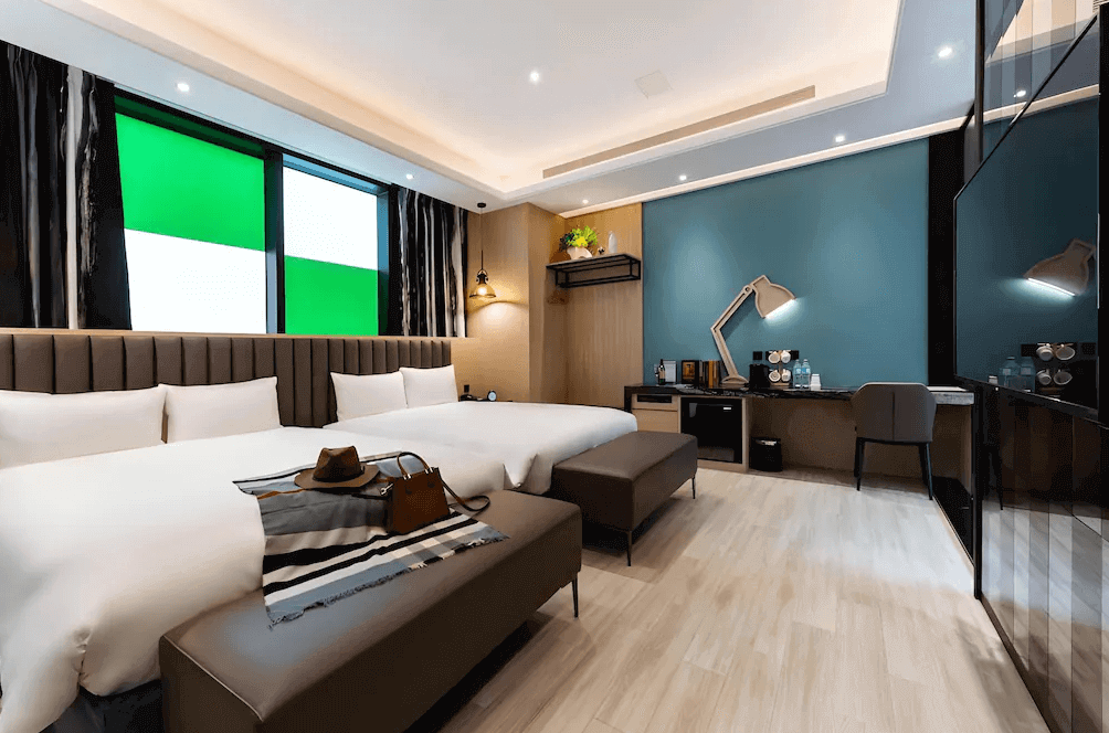 【台中火車站住宿】「挪威森林台中文創館的現代雙床客房，採用清新藍綠主牆、木質調設計與全景窗戶，搭配舒適大床、長凳與辦公桌，營造明亮又時尚的住宿氛圍。」